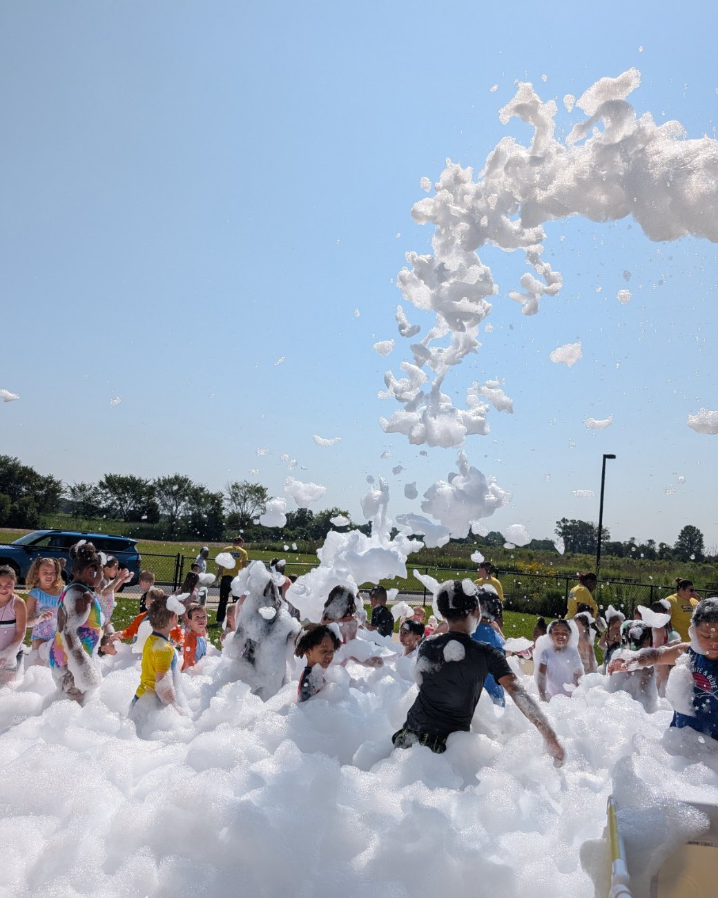 A Party Foam event in full swing, a foam cannon arcing over a field of foam and dozens of kids playing